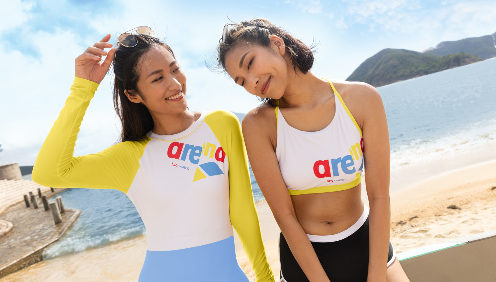An outdoor creative shoot showcasing 2 female models wearing Arena swimsuit with a beach background. Photographed by I Heart Studios.