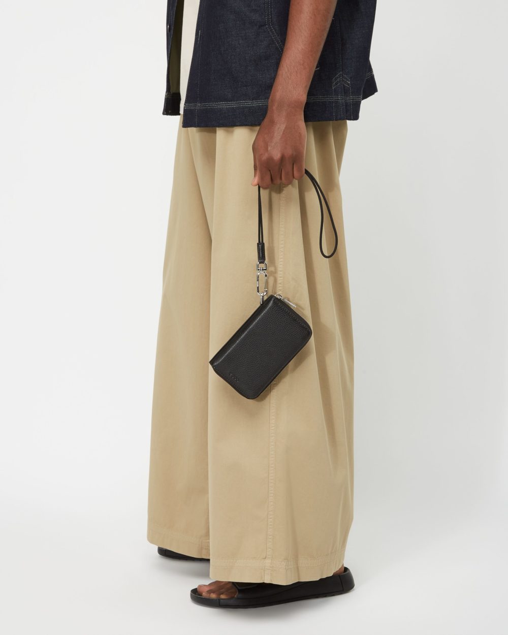 A lookbook fashion close up image featuring a man wearing a fashionable outfit holding a bag with his hand in front of a white background. Photographed by I Heart Studios.