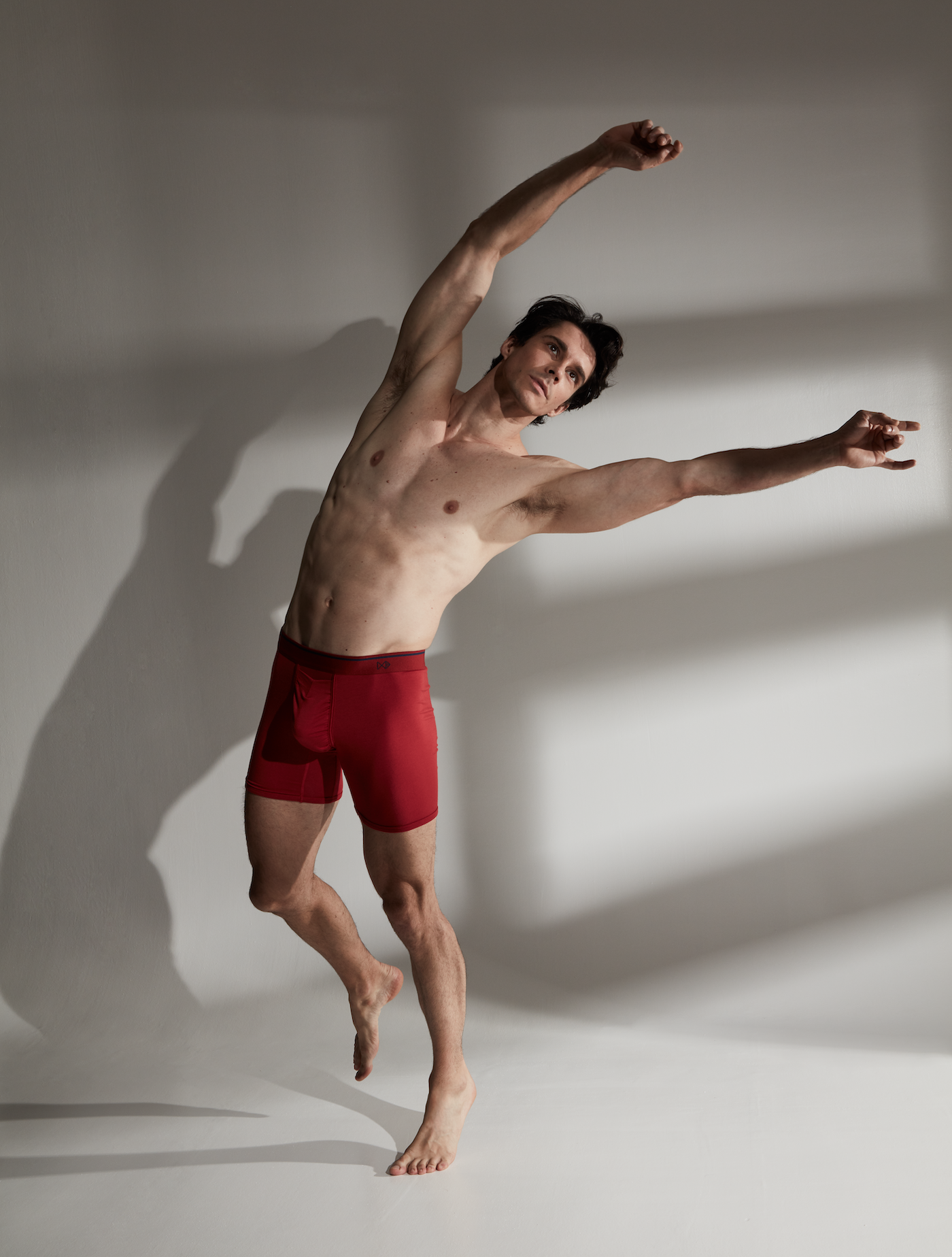 A man wearing red shorts dancing in front of a white background with a shadow. Creative promotional image captured by I Heart Studios.
