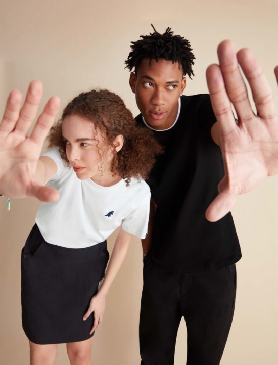 A male and a female model posing with confidence and raising their hands in a stop sign gesture against a cream-colored backdrop. Model fashion photo photographed by I Heart Studios.