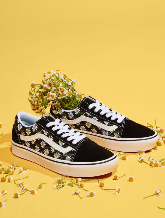 An image of black Vans sneakers with a floral pattern, adorned with a bunch of small yellow flowers against a vibrant yellow background, showcasing a fresh and vibrant vibe. Creative product image photographed by I Heart Studios.